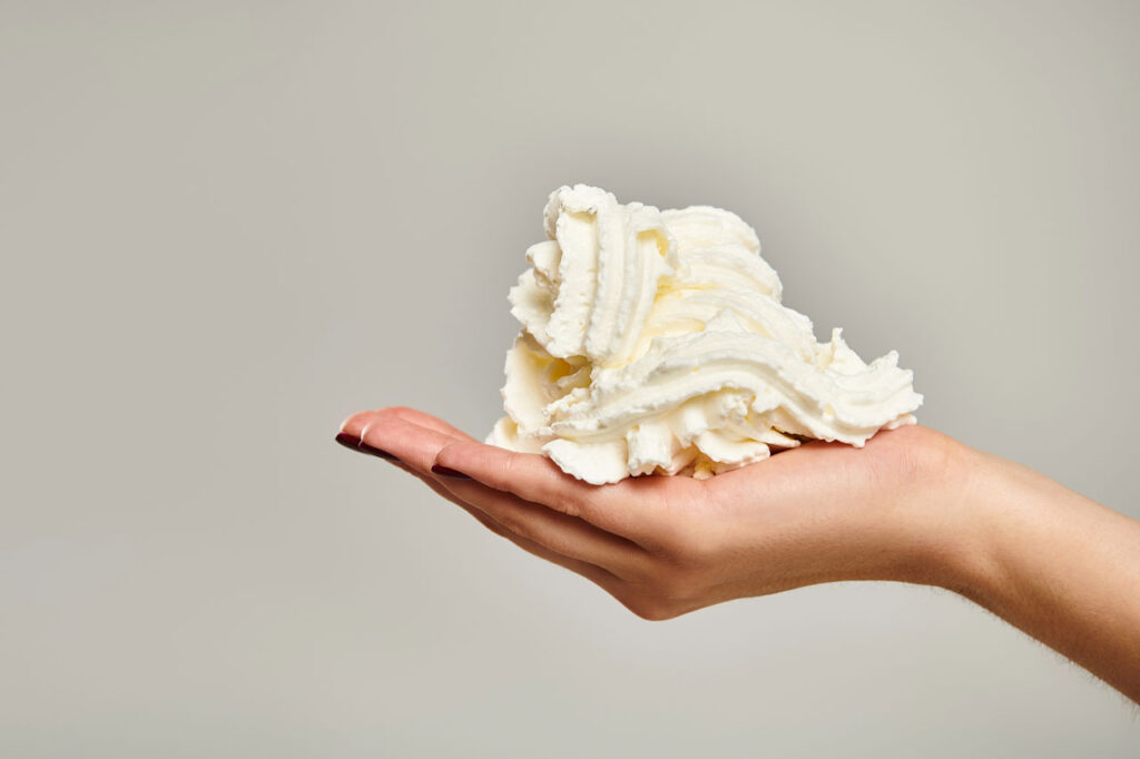 A hand holding a mountain of thick, velvety n20 whipped cream Owasso against a clean, neutral background.