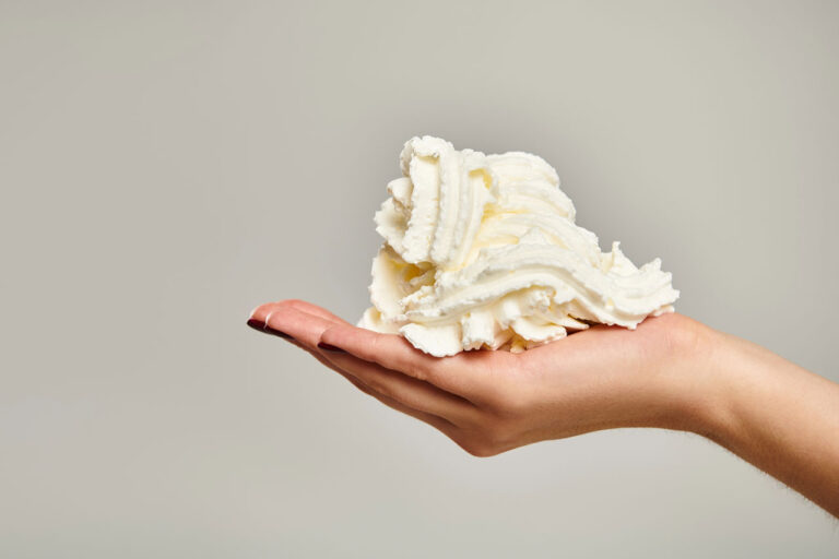 A hand holding a mountain of thick, velvety n20 whipped cream Owasso against a clean, neutral background.