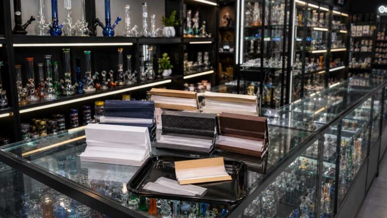 Premium rolling papers Broken Arrow selection displayed on a glass store counter with bongs in the back.