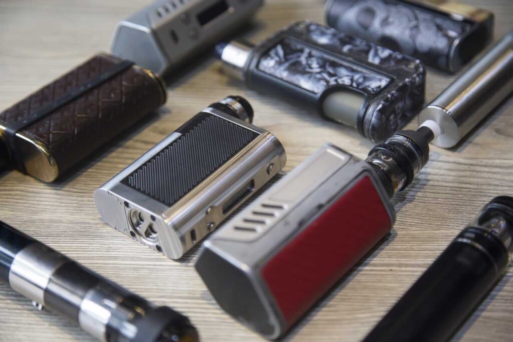 A premium collection of high-end box vape mods and sub-ohm tanks displayed on a wooden table at a vape mods Tulsa shop.