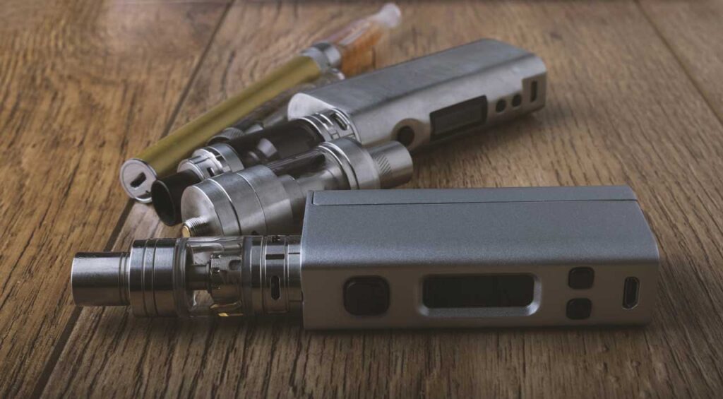 A variety of sleek metallic box vape mods with glass tanks and an e-cigarette pen from a top vape mods Tulsa supplier.