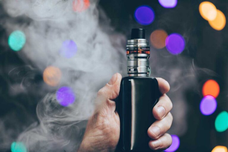 Premium box mod vape from a vape store Broken Arrow. Hand holding device with clouds and colorful bokeh background.
