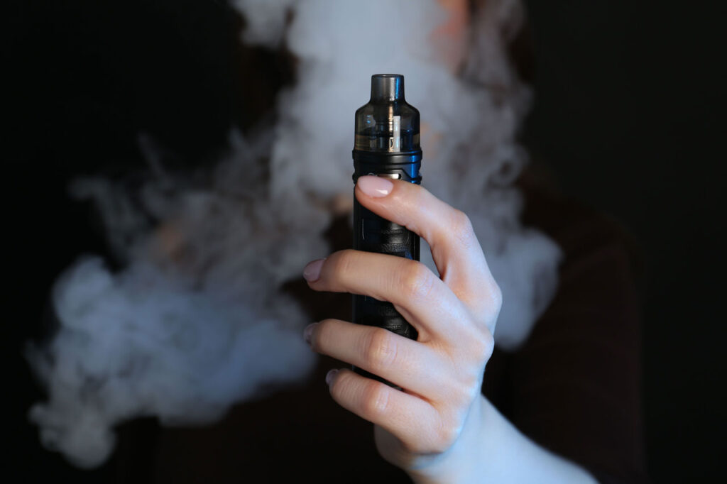 Modern pod mod system from a local vape store Broken Arrow. Hand holding a compact black pod vape with dense vapor.