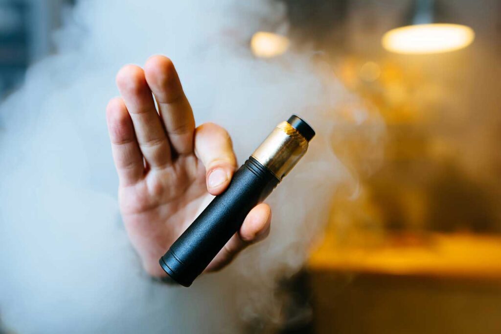 Sleek vape pen available at a vape store Broken Arrow. Person holding a black and gold vape device amid thick smoke.