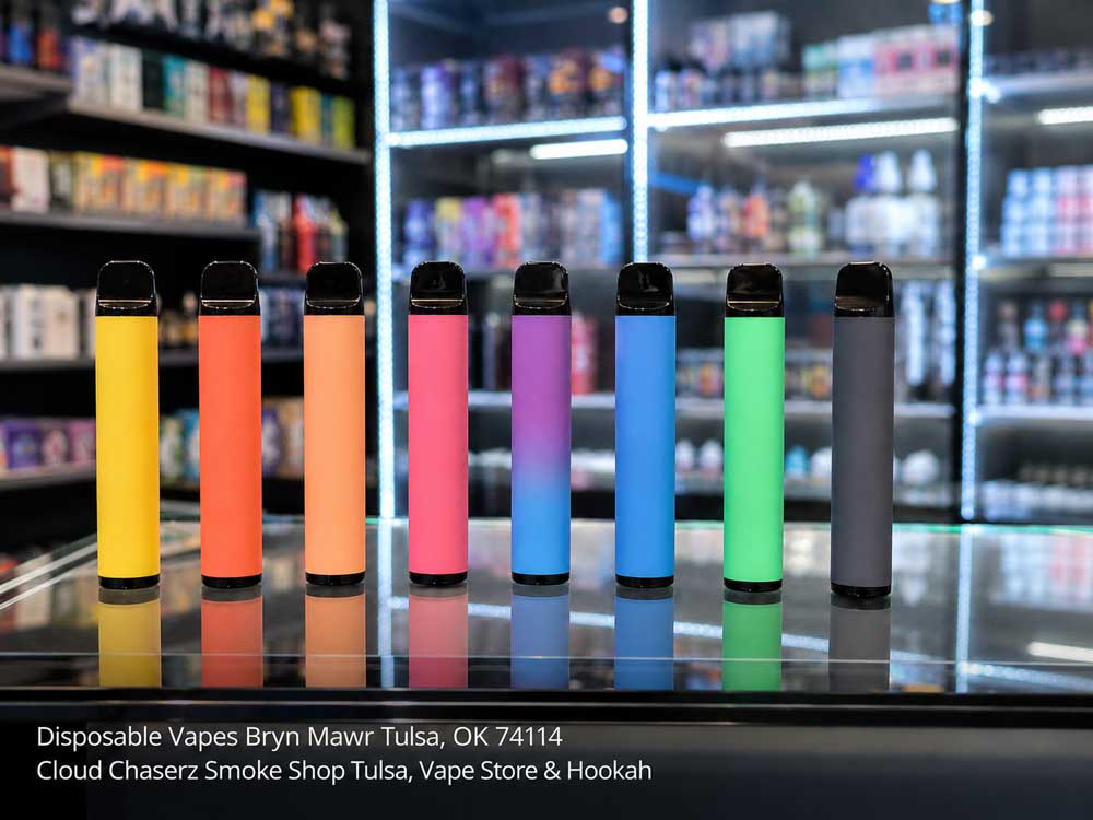 Selection of colorful disposable vapes Tulsa lined up neatly on a glass counter inside a brightly lit smoke shop.