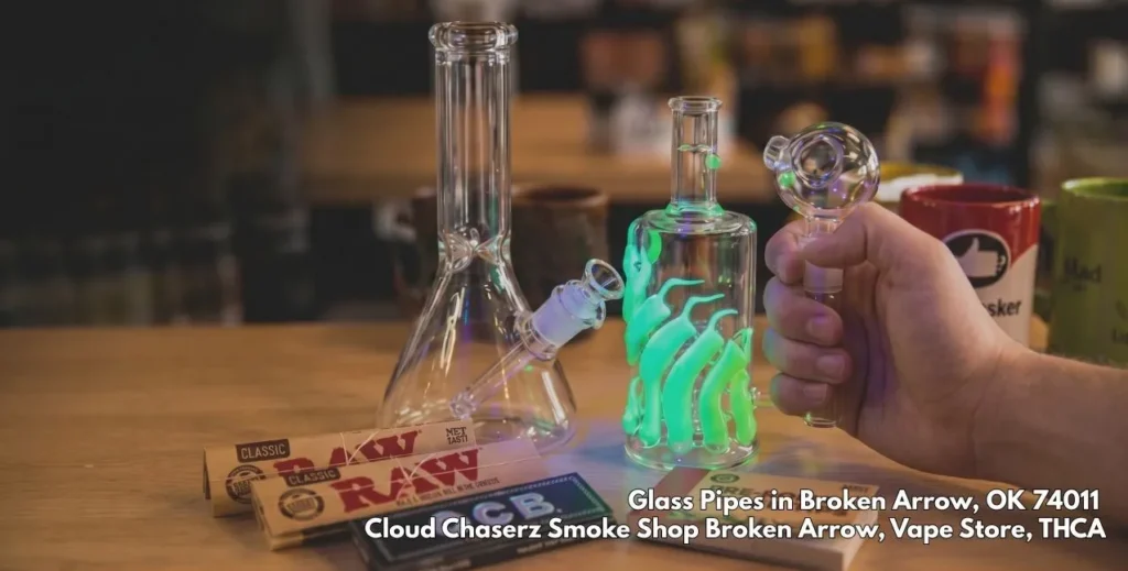 Clear water bongs, a glowing rig, rolling papers, and premium glass pipes Broken Arrow on a wooden display table.